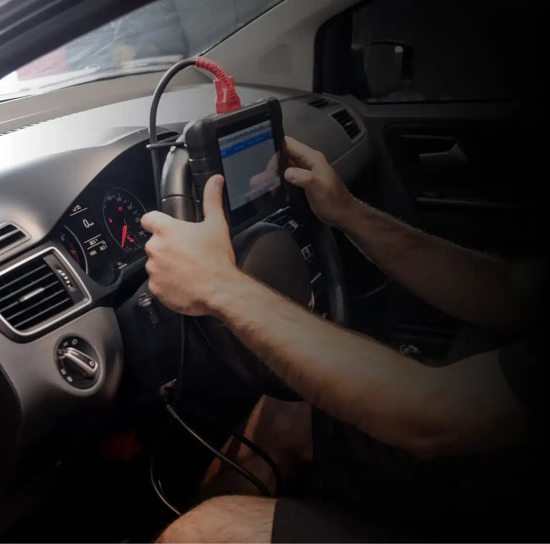 A person uses a diagnostic scanner connected to a car’s dashboard, holding the device with both hands while sitting in the driver’s seat.