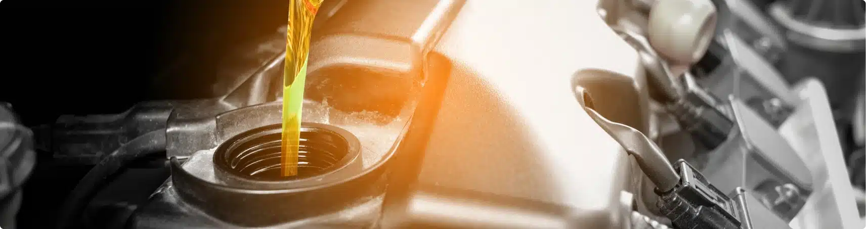 Golden motor oil being poured into the oil fill opening of a car engine, with engine components visible in the background.