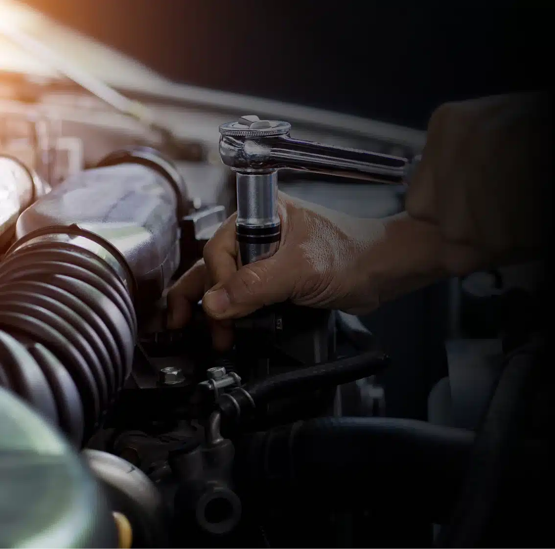 A close-up of a person using a ratchet wrench to tighten a bolt under the hood of a car, with engine components visible and hands in focus.