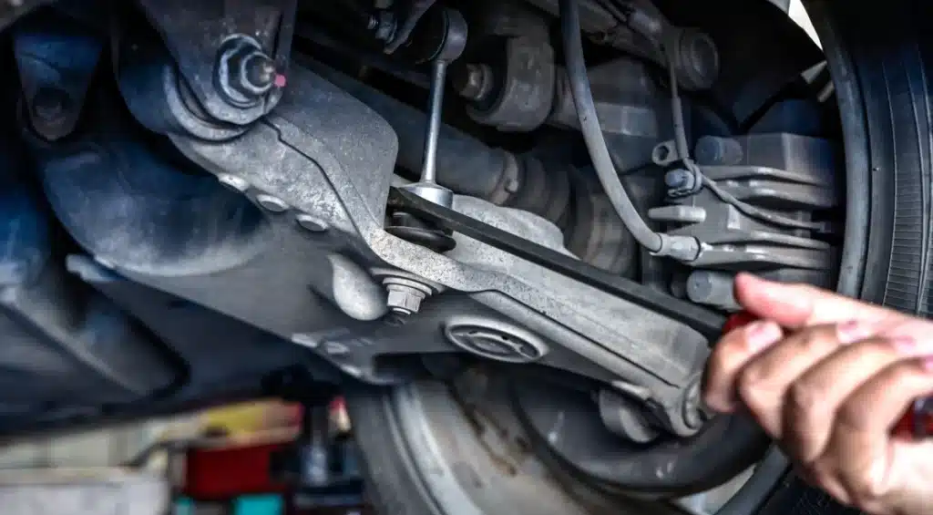 A close-up of a mechanics hand using a tool to work on a cars suspension system, showing various metal components and a tire.
