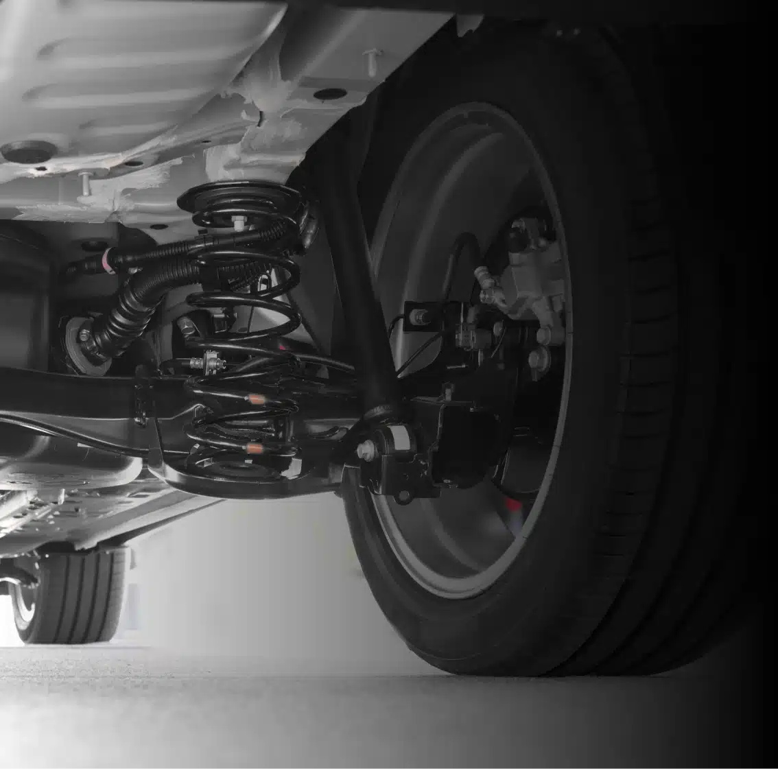 Close-up view of a car’s rear suspension system, showing the coil spring, shock absorber, and tire underneath the vehicle, with detailed mechanical components visible.