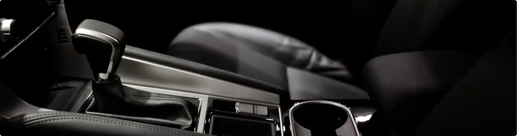 Close-up view of a cars center console featuring the gear shift, cup holder, and armrest in a modern, black interior.