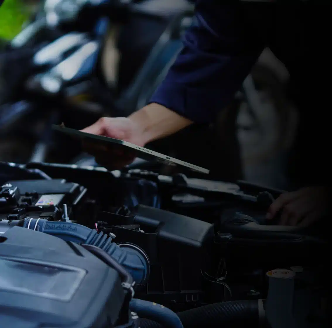 Preventative maintenance in Des Moines, IA shown with person in dark clothing checks a clipboard while inspecting the engine of a car, with the vehicle’s hood open and engine components visible.