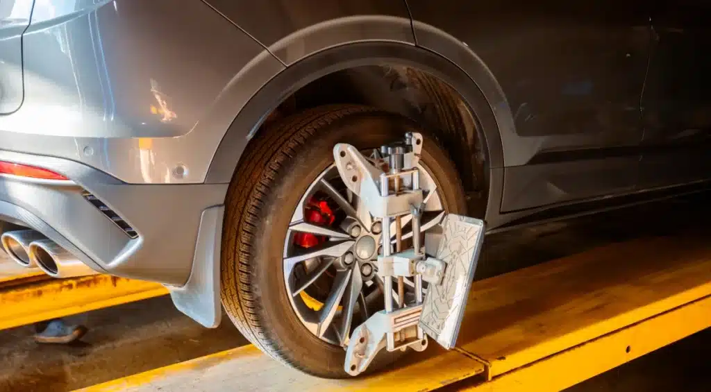 A close-up of a car’s rear wheel on a yellow lift, fitted with an alignment tool, indicating that a wheel alignment service is being performed in an auto repair shop.