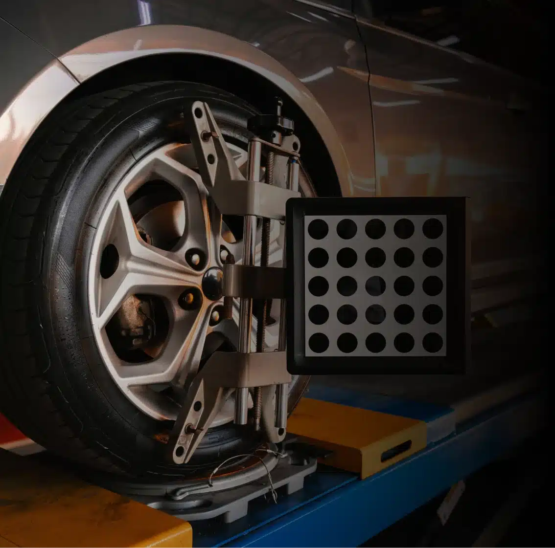 Preventative maintenance in Des Moines, IA shown with Close-up of a car wheel on an alignment machine with a calibration target attached, positioned on a vehicle lift in an auto repair shop.